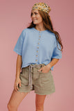 Woman wearing a blue shirt and green shorts with a floral headband on a pink background