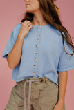 Woman wearing a light blue button-up shirt and green shorts against a pink background