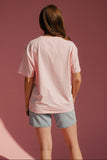 Person wearing a pink oversized t-shirt and denim shorts against a pink background