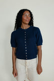 Woman wearing a navy blue short-sleeve cardigan with white buttons on a plain background