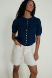 Woman wearing a navy blue button-up shirt and white shorts against a plain background