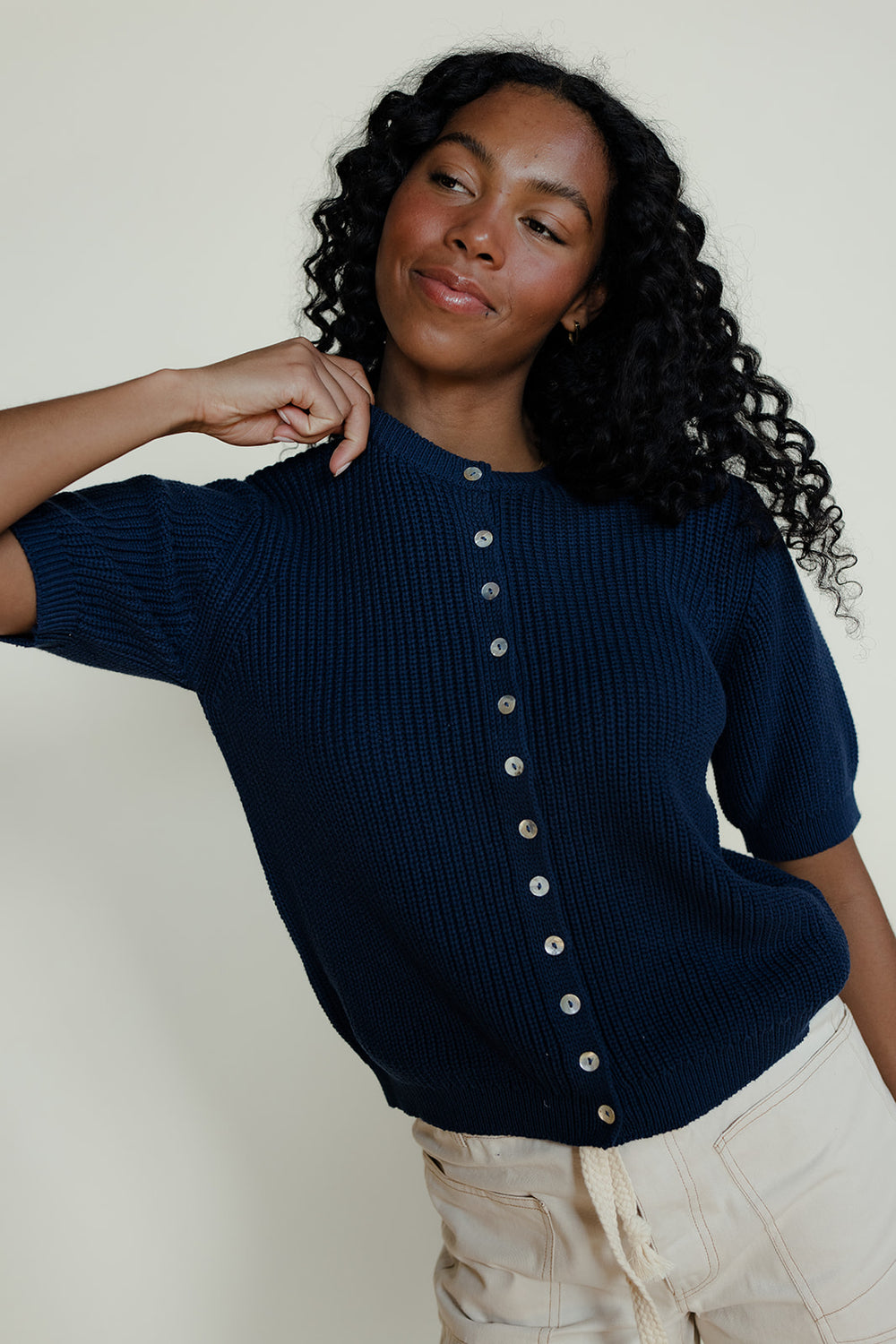Woman wearing a navy blue ribbed sweater with buttons against a plain background
