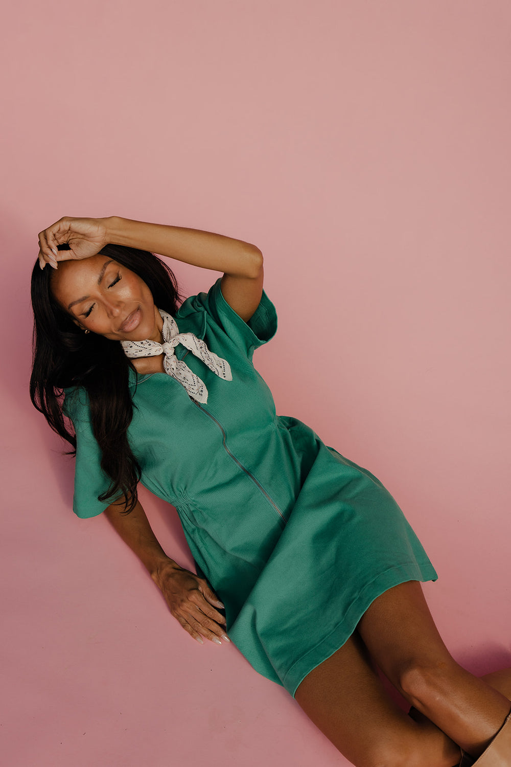 Woman in a green dress posing against a pink background