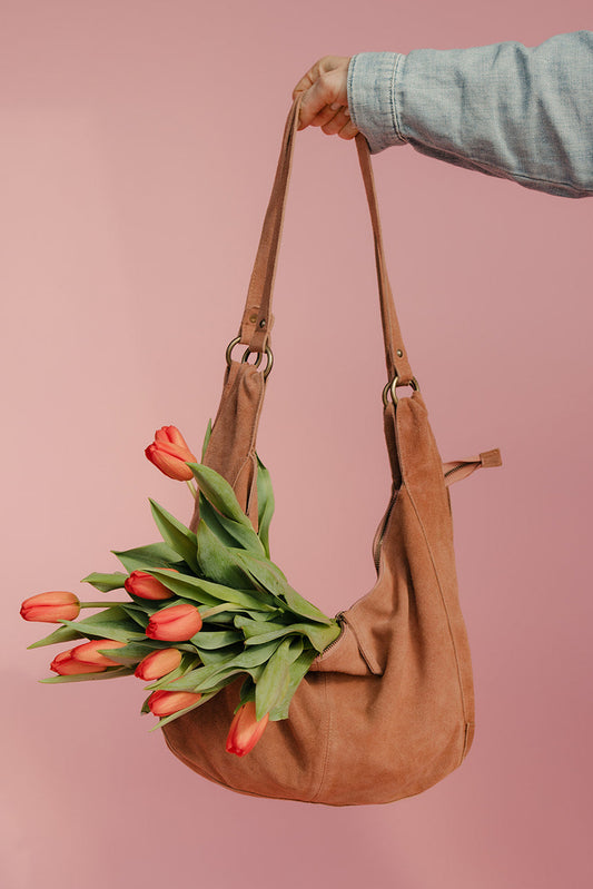 Brown leather handbag with red tulips against a pink background