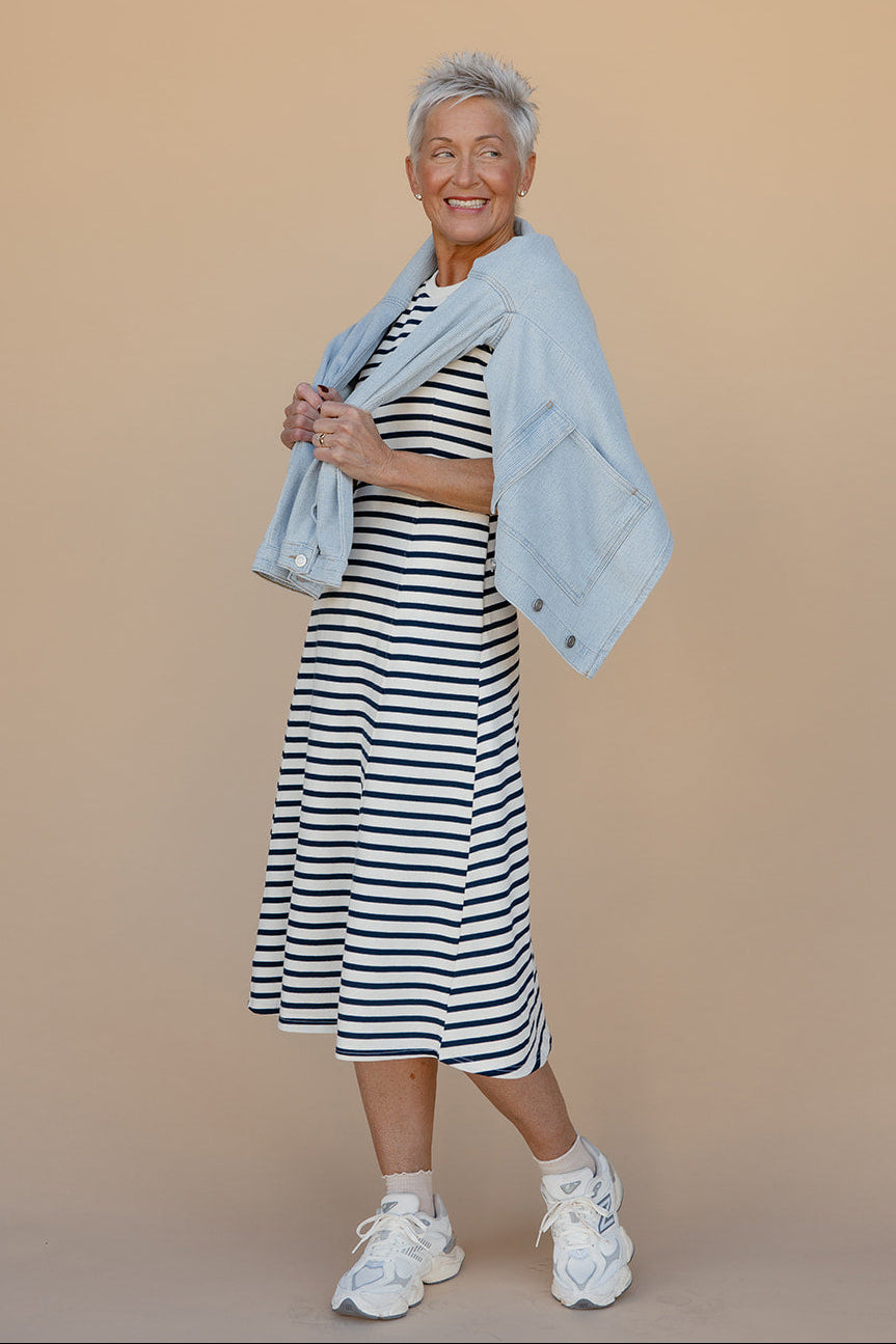 Woman wearing a striped dress and light jacket against a beige background