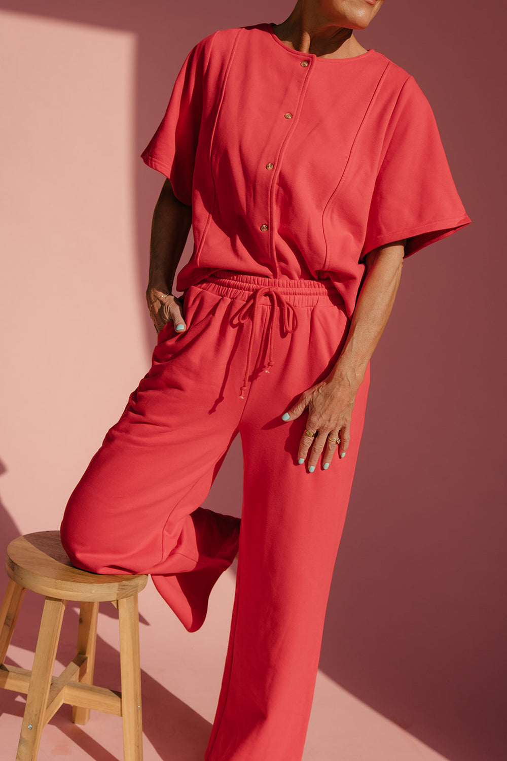 Person wearing a red outfit standing on a wooden stool against a pink background