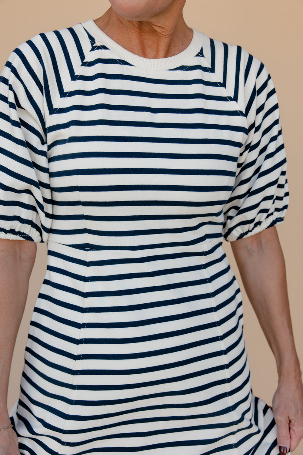 Person wearing a white and navy striped dress against a beige background