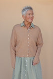 Woman wearing a brown cardigan over a green checkered shirt and skirt against a beige background