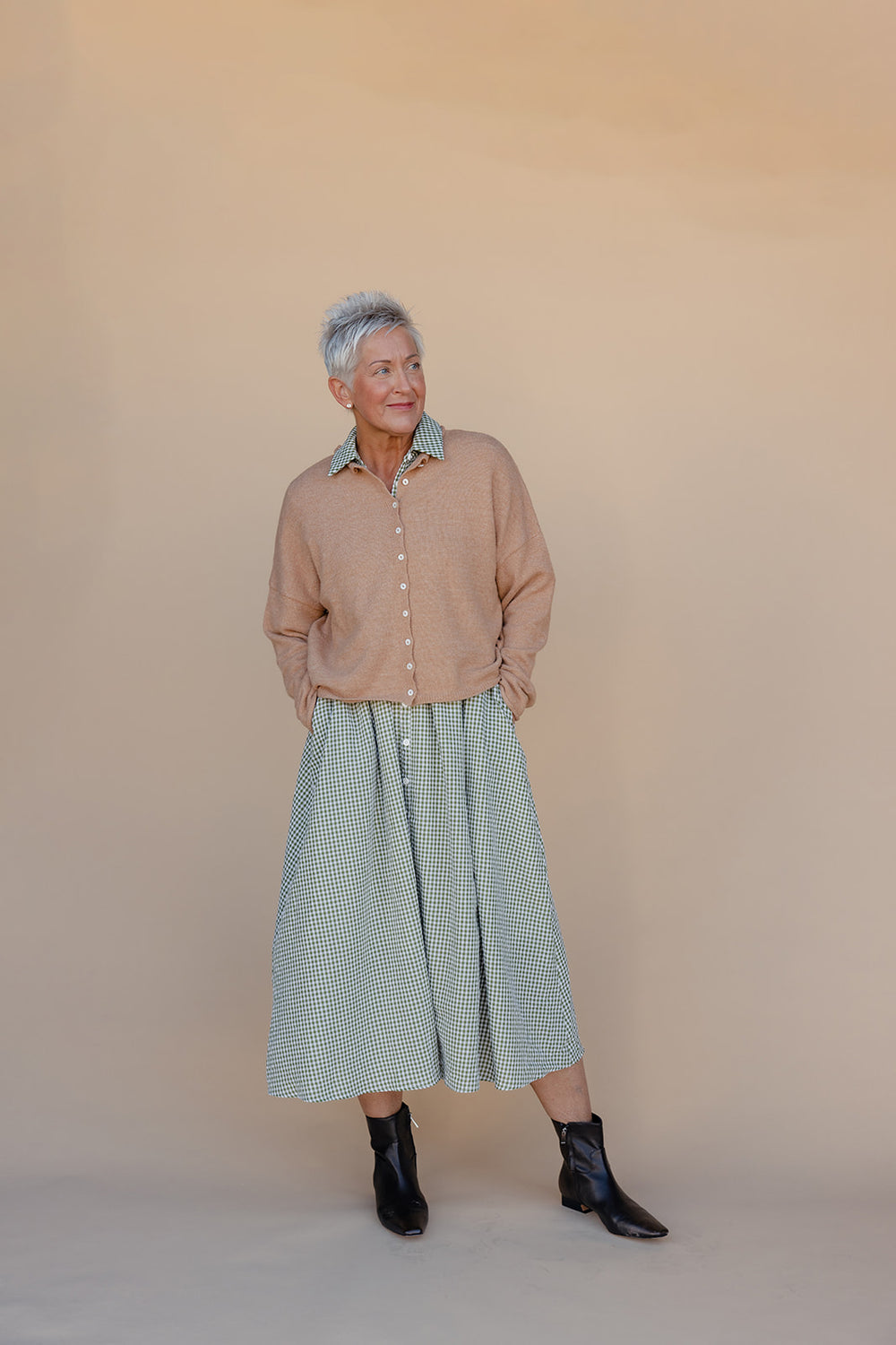 Woman wearing a beige shirt and green checkered skirt against a plain background