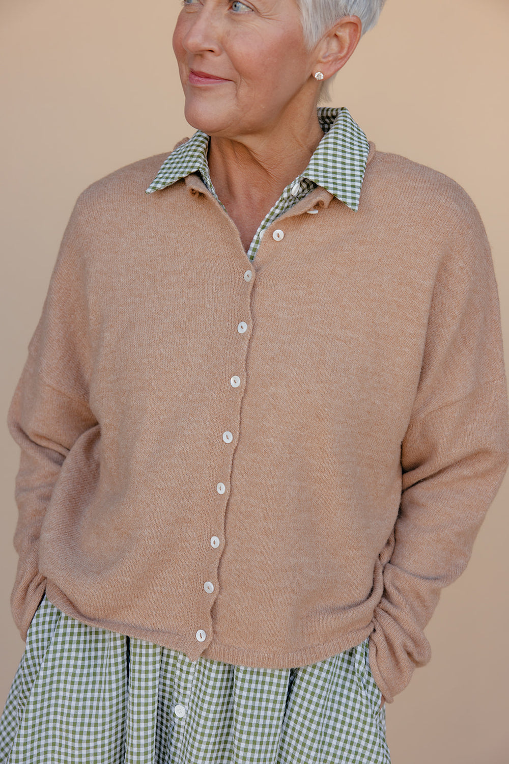 Woman wearing a beige cardigan over a checkered shirt against a beige background
