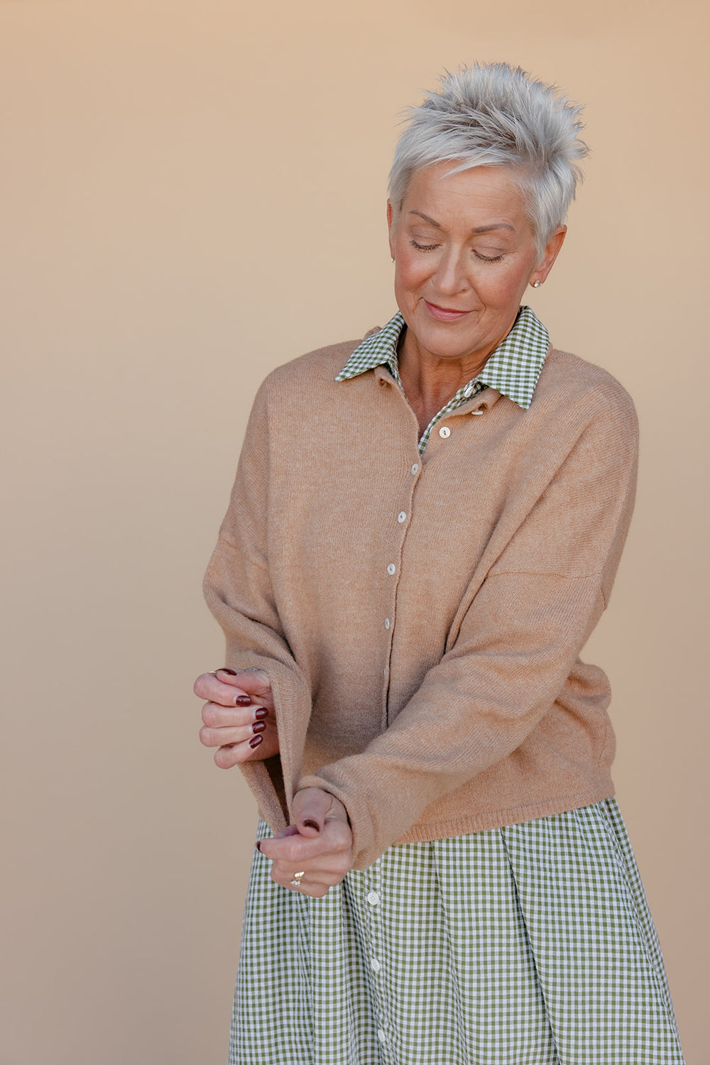 Woman wearing a brown cardigan over a green checkered dress on a beige background