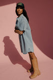 Woman wearing a denim dress, brown boots, and a green cap on a pink background