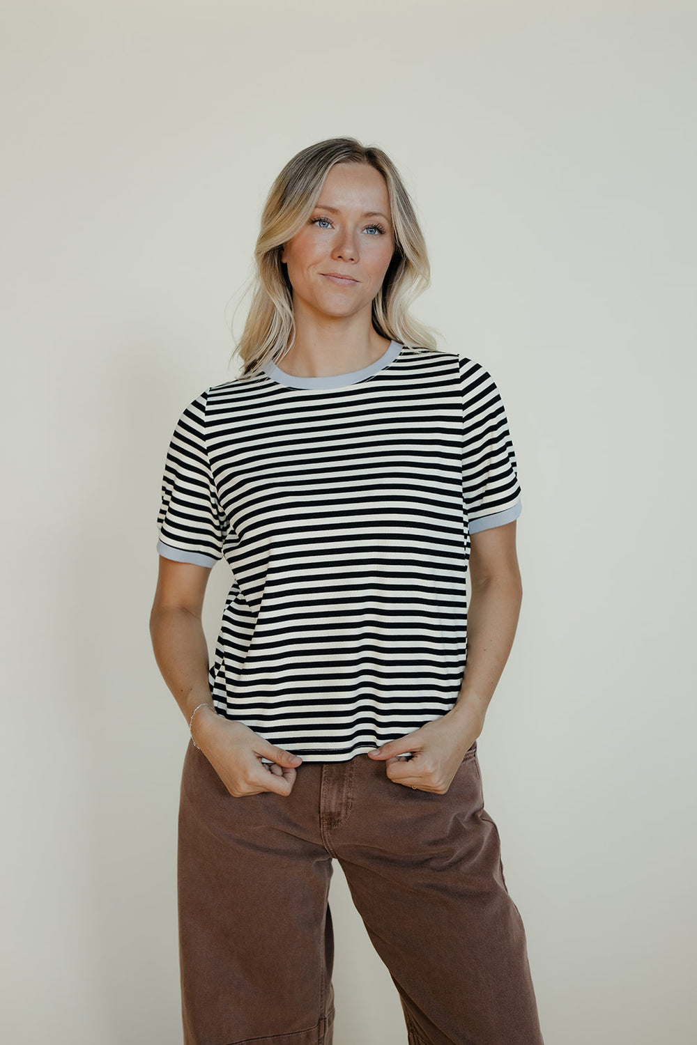 Woman wearing a black and white striped shirt and brown pants against a plain background