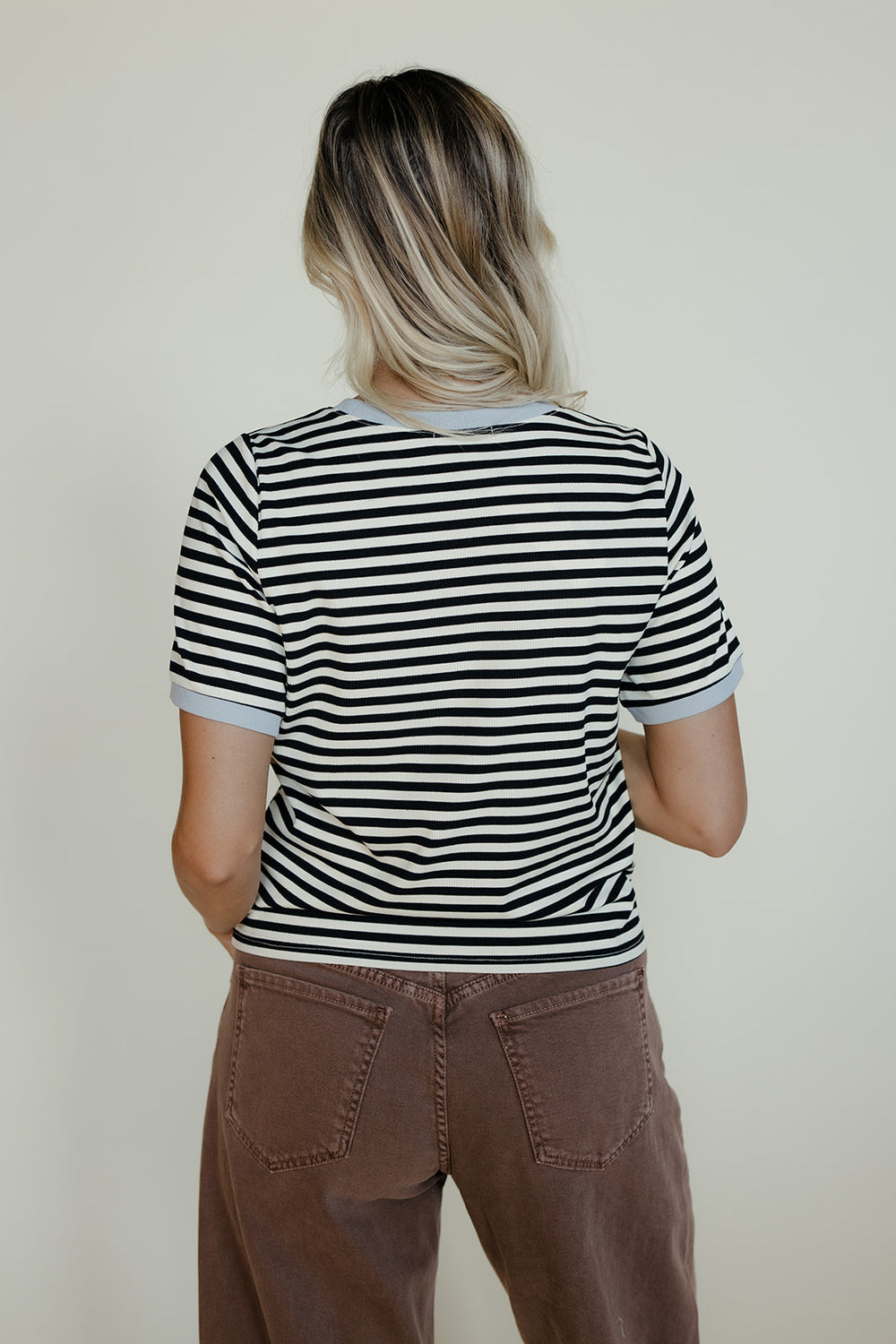Person wearing a black and white striped shirt with brown pants on a plain background