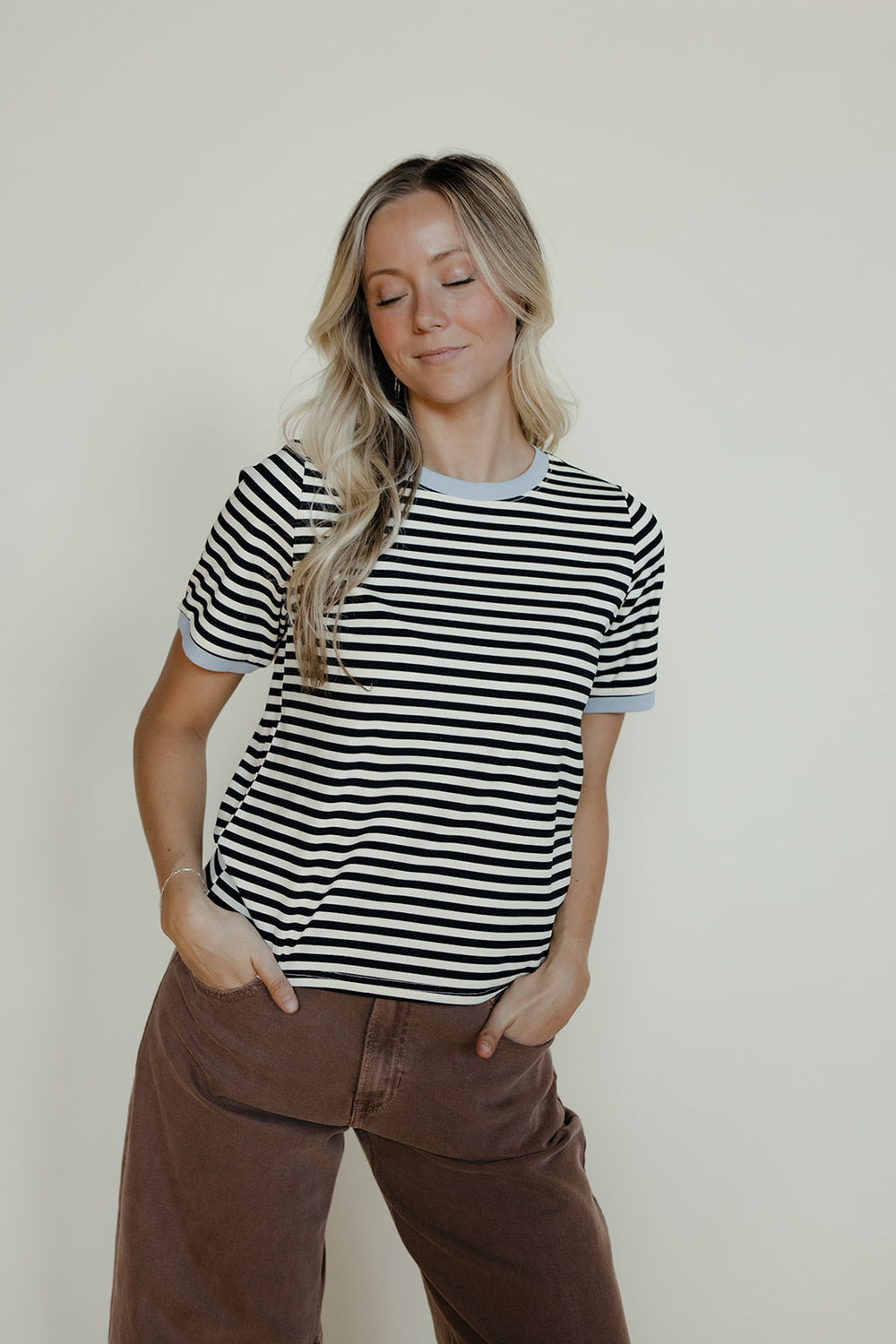 Woman wearing a black and white striped shirt and brown pants against a plain background