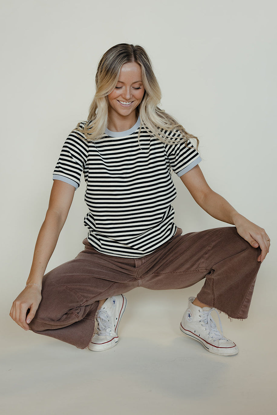 Woman sitting on the floor wearing a striped shirt and brown pants against a plain background