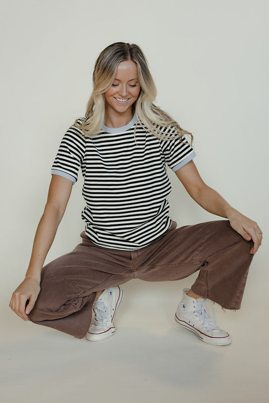 Woman sitting on the floor wearing a striped shirt and brown pants against a plain background
