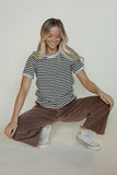 Woman sitting on the floor wearing a striped shirt and brown pants against a plain background
