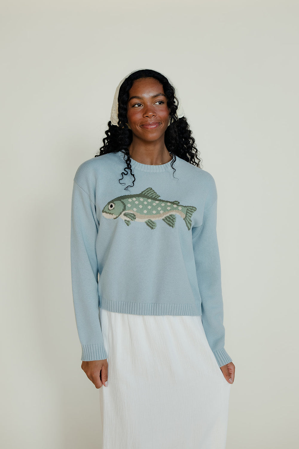 Woman wearing a light blue sweater with a fish design against a white background