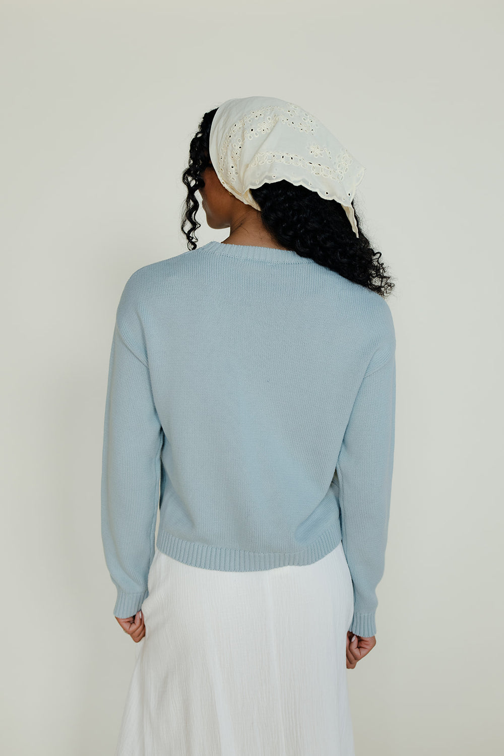 Person wearing a light blue sweater and white pants against a plain background