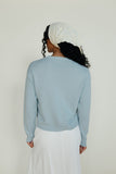 Person wearing a light blue sweater and white pants against a plain background