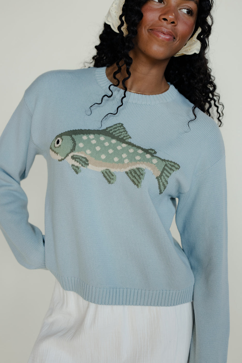 Person wearing a light blue sweater with a fish design against a plain background