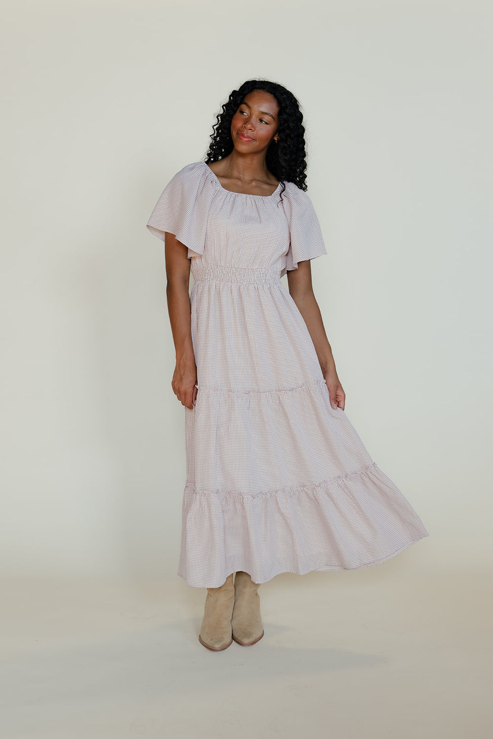 Woman wearing a light-colored dress with ruffled sleeves against a white background
