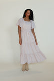 Woman wearing a light-colored dress with ruffled sleeves against a white background