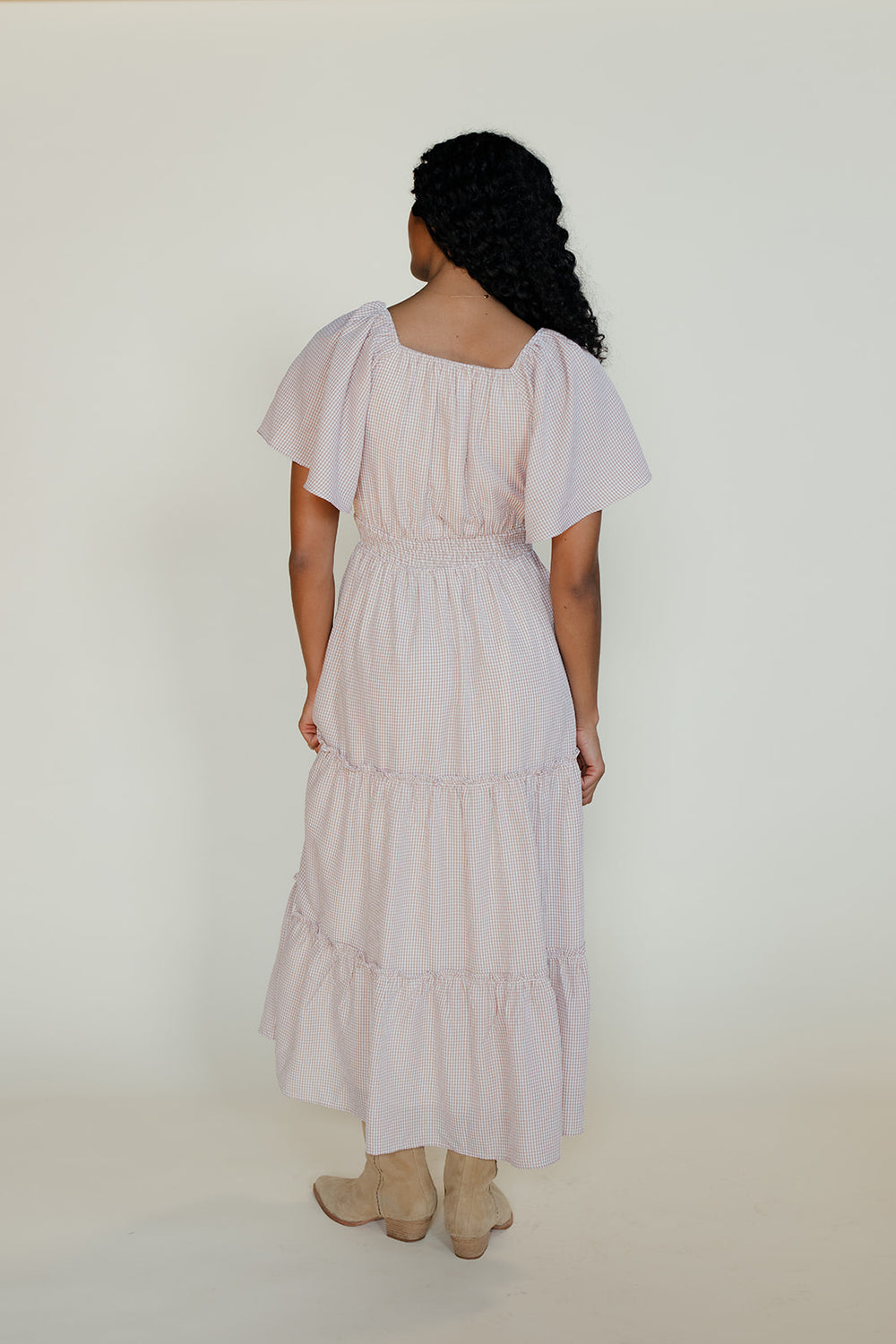 Woman wearing a light pink dress with tiered skirt and short sleeves on a white background