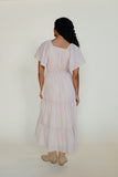 Woman wearing a light pink dress with tiered skirt and short sleeves on a white background