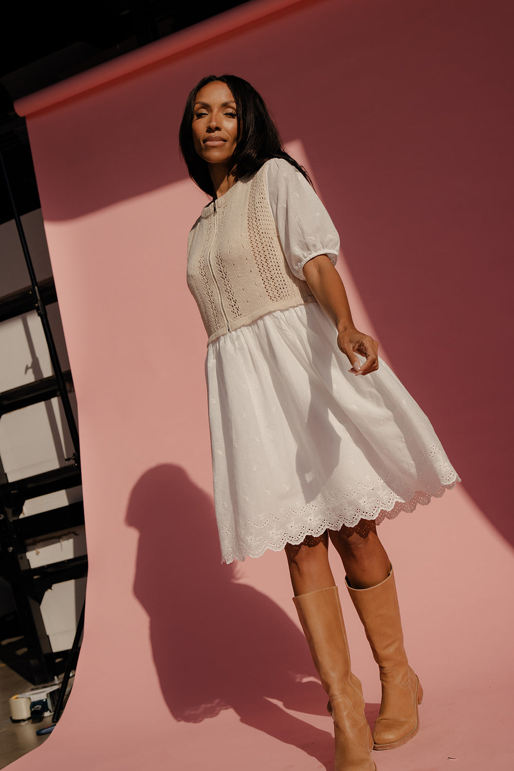 Woman wearing a white dress and brown boots against a pink background