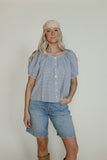 Woman wearing a light blue blouse and denim shorts against a plain background