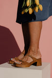 Person wearing brown sandals on a white platform with a pink background