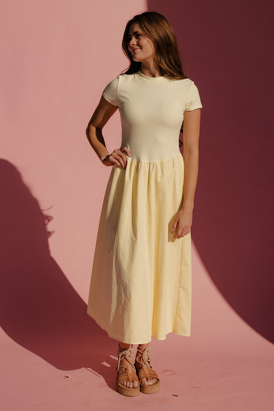 Woman in a yellow dress standing against a pink background