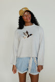 Woman wearing a white sweatshirt with a design, light blue shorts, and a yellow cap against a plain background