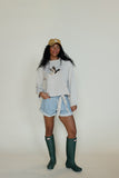 Person wearing a light gray sweatshirt, denim shorts, and green rain boots against a white background