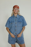 Person wearing a denim outfit with a red bandana on a plain background