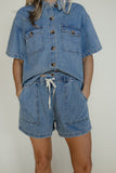 Person wearing a matching denim outfit with a shirt and shorts on a plain background