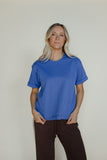 Woman wearing a blue t-shirt and brown pants against a plain background