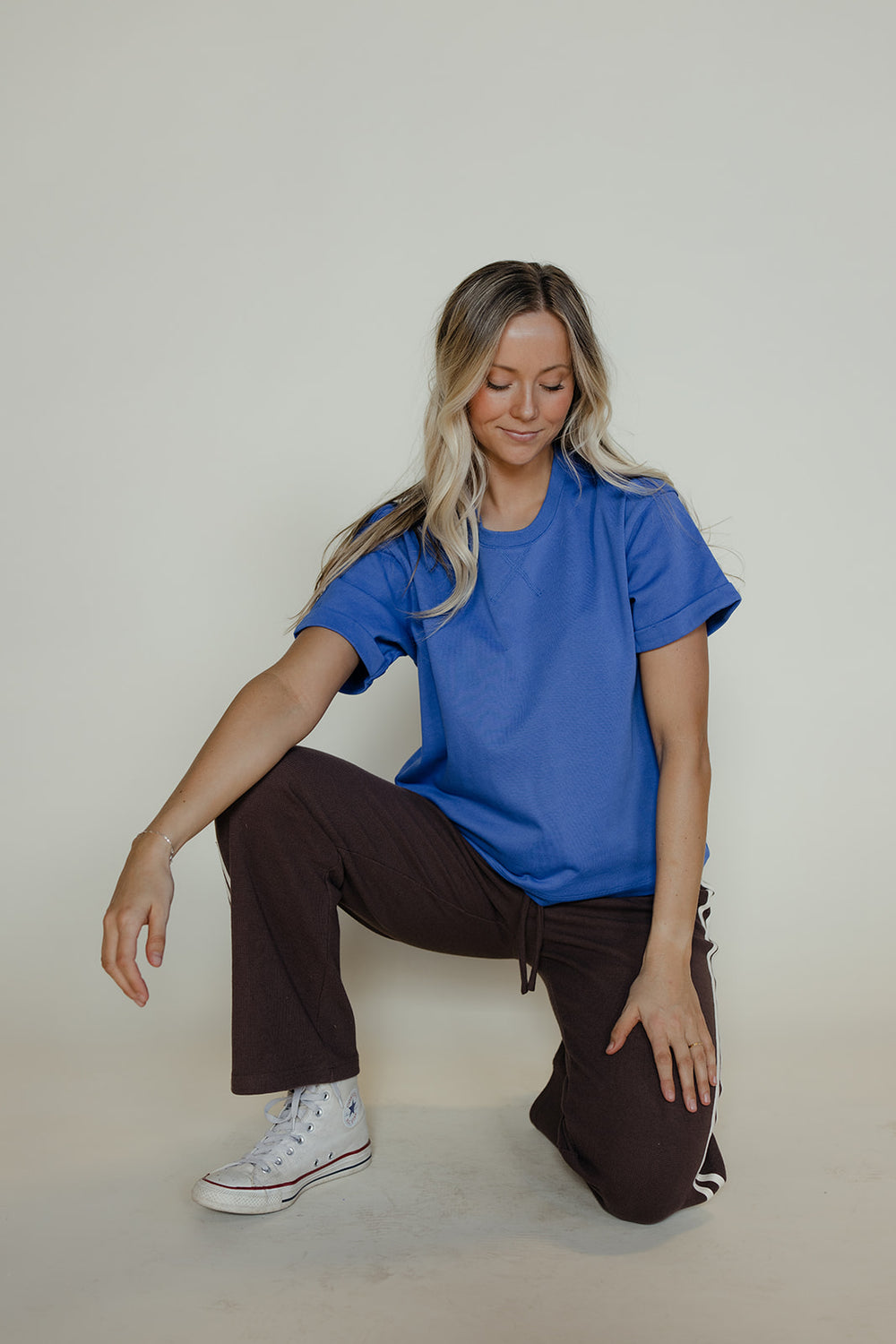 Woman wearing a blue t-shirt and brown pants sitting on a white floor.