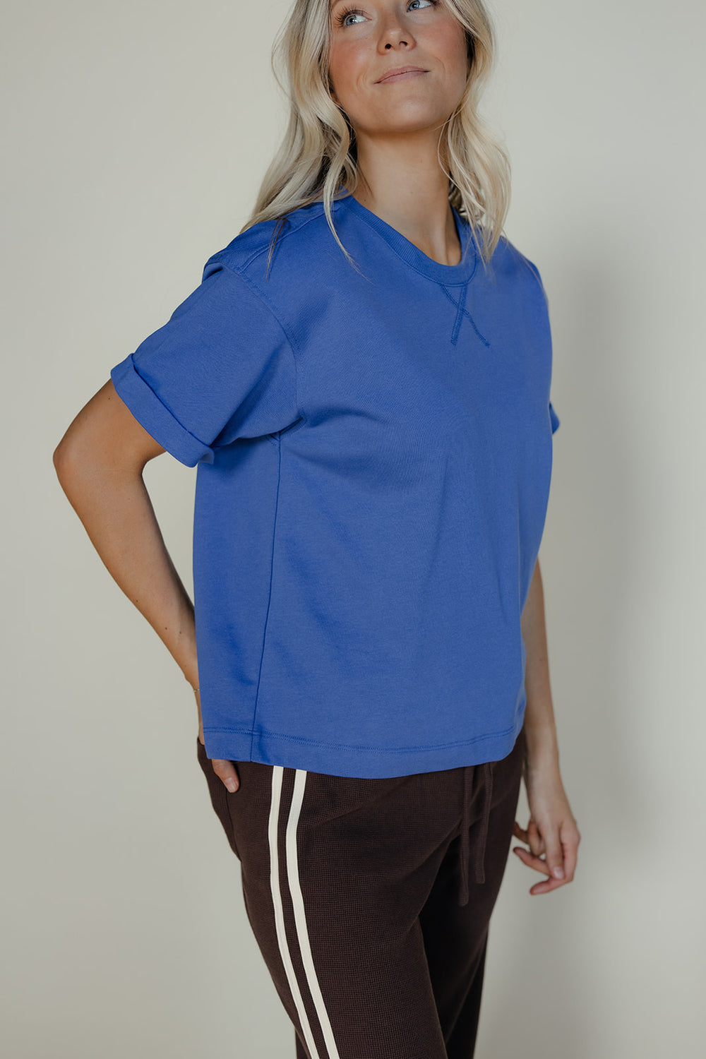 Person wearing a blue oversized shirt and brown pants with white stripes on a plain background