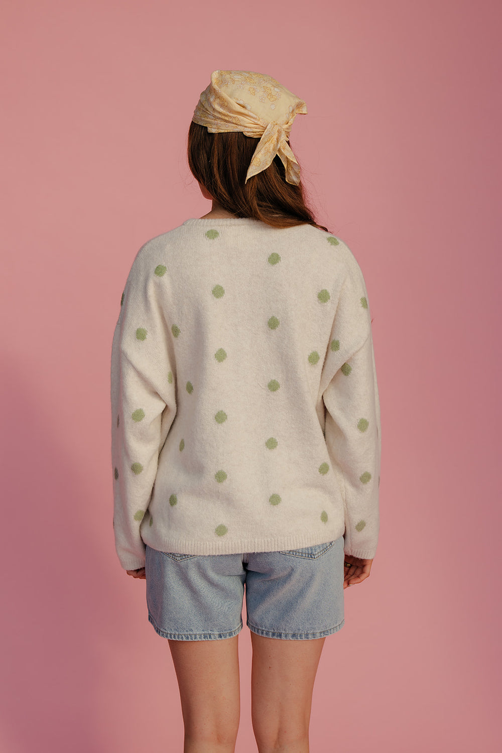 Person wearing a polka dot sweater and denim shorts with a pink background