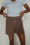 Person wearing a light blue shirt and brown shorts against a plain background