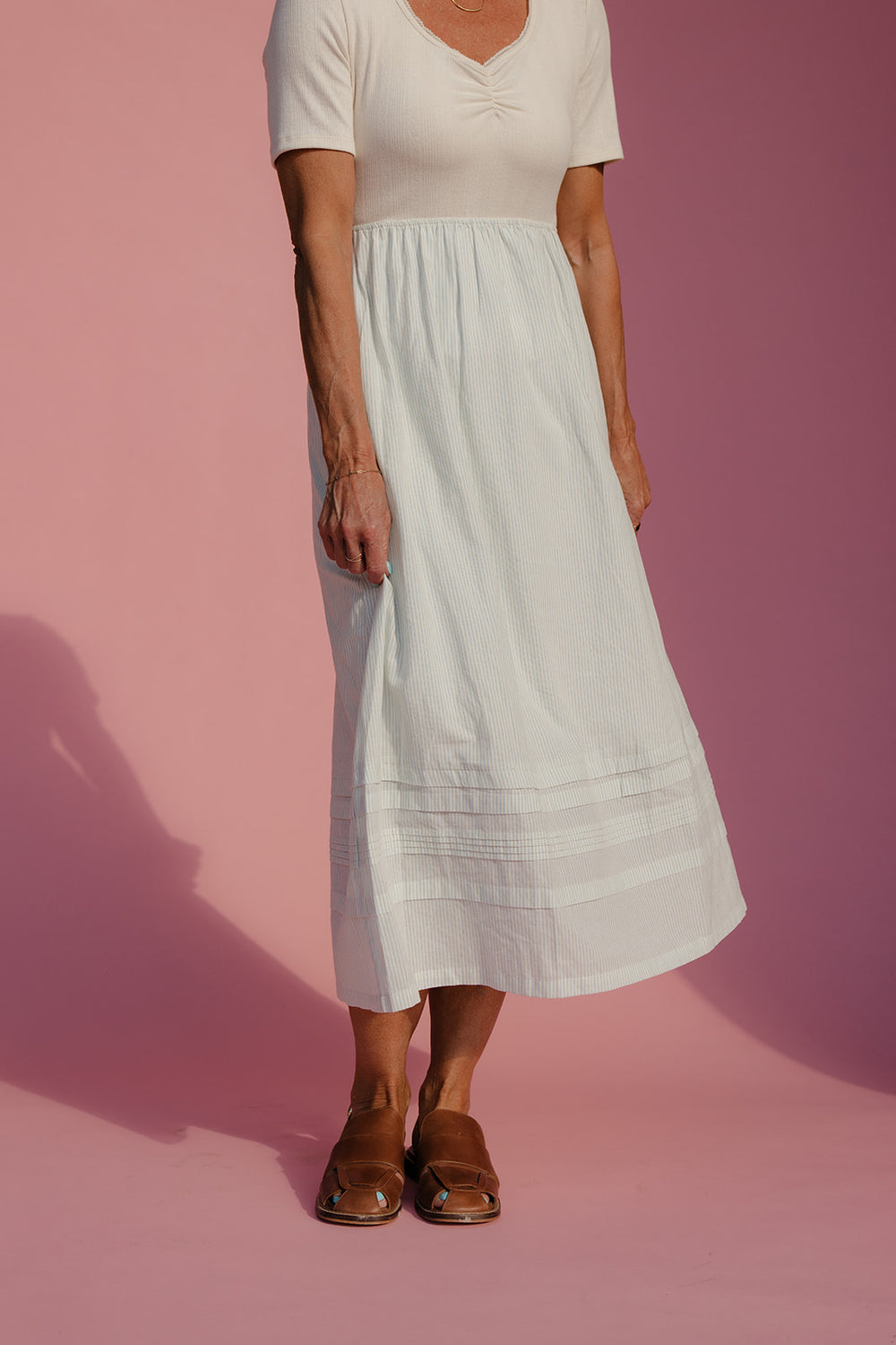 Person wearing a white top and light blue skirt on a pink background