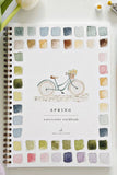 Spring watercolor workbook with a bicycle illustration and color swatches on a white background.