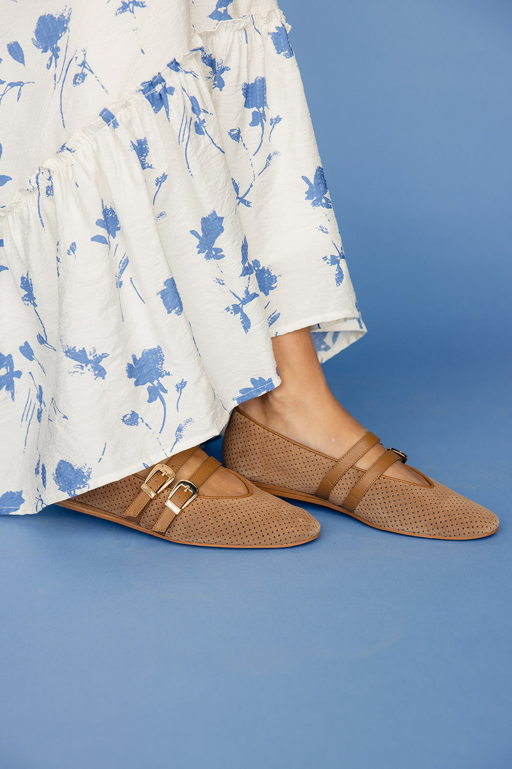 Brown sandals worn with a white floral dress on a blue background
