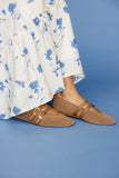 Brown sandals worn with a white floral dress on a blue background