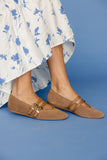 Brown woven shoes with buckles worn with a white floral dress on a blue background