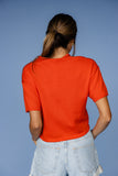 Person wearing an orange t-shirt and light blue jeans against a blue background