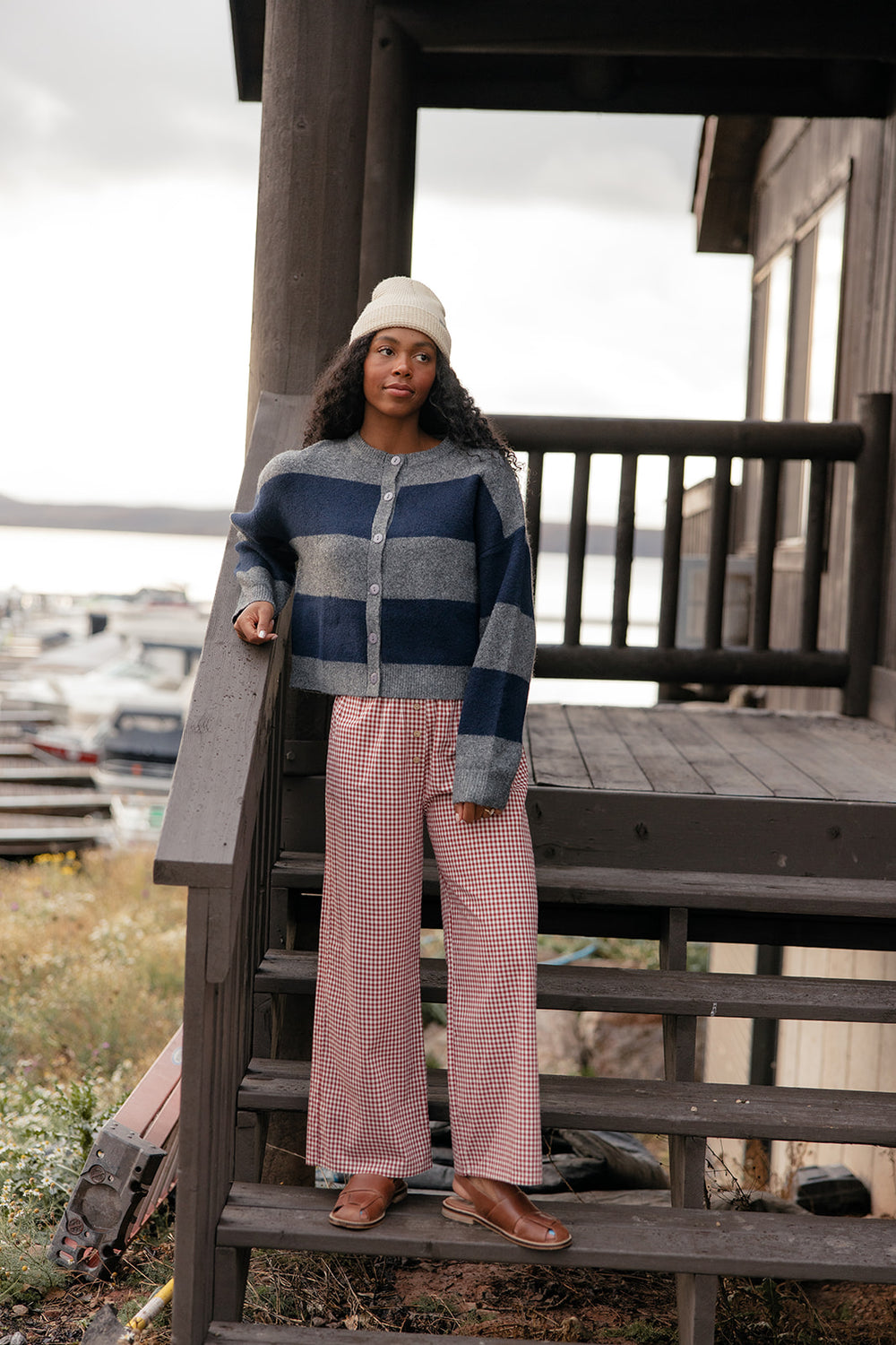 Woman standing on a wooden staircase wearing a striped sweater and pink pants with a scenic background.